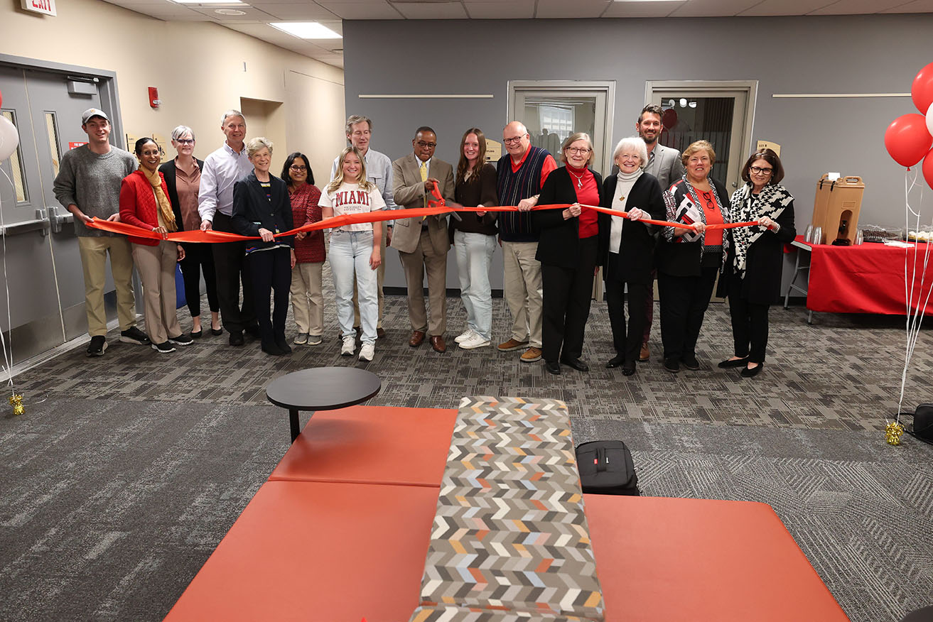 All Ribbon Cutting participants stand in a line holding the red ribbon. Dean Conley - in the middle of the line - holds red scissors and prepares to cut the ribbon.